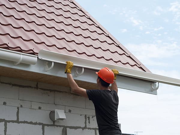 worker installing gutter system on roof